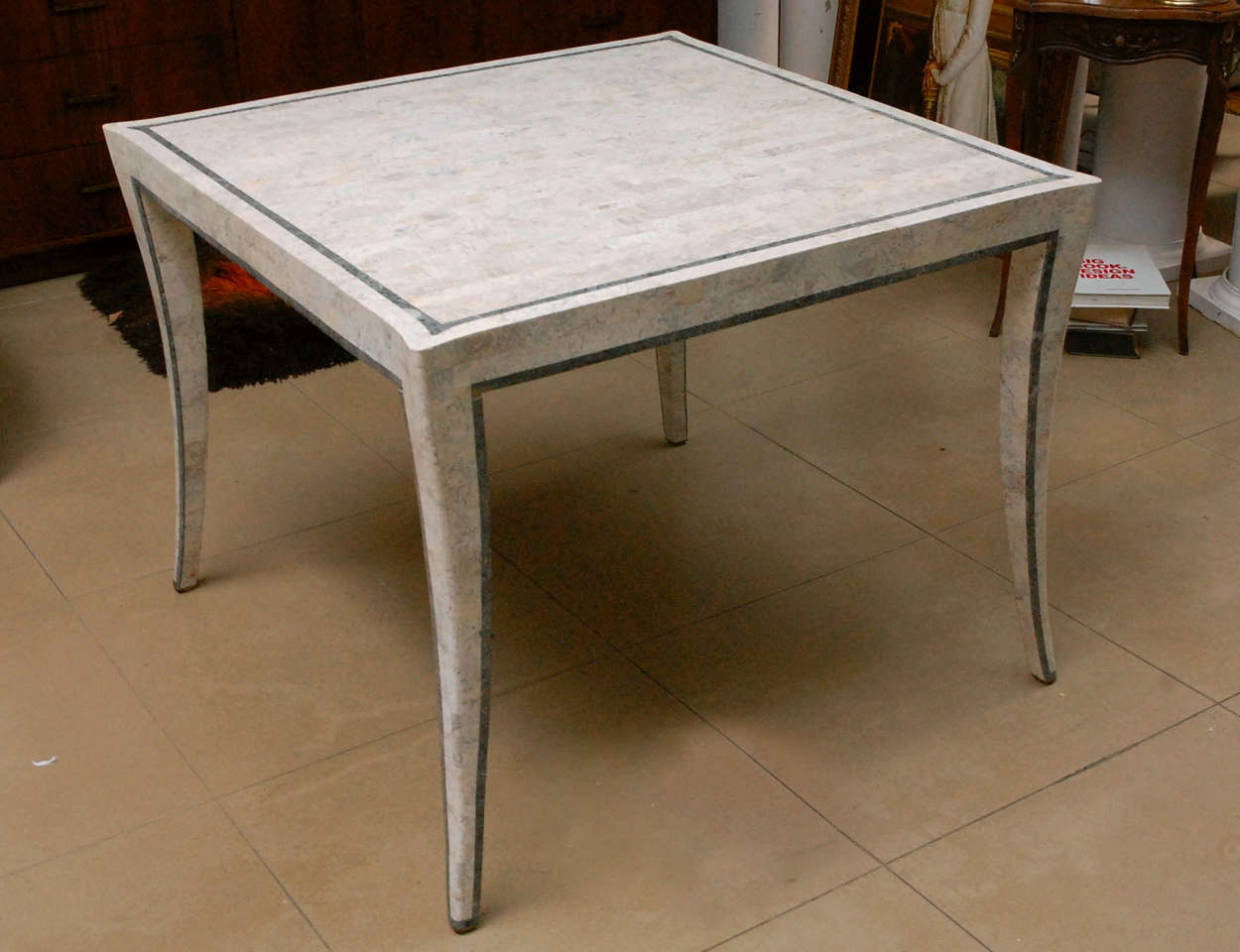 Tesselated marble square dining table in shades of cream with gray inlay square in table top and gray trim on legs. Legs have elegant curve.