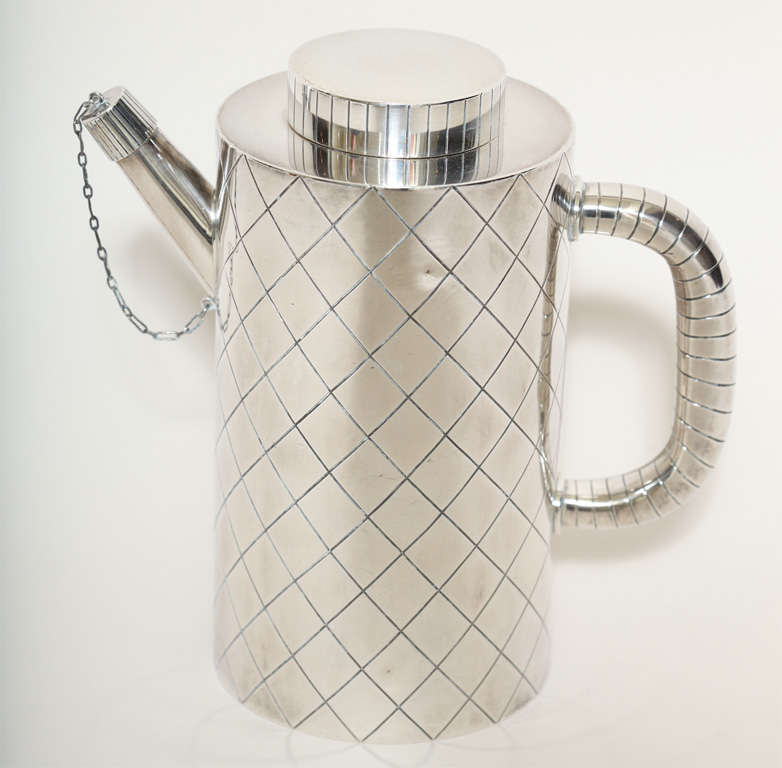 This cocktail shaker is cylindrical with an engraved lozenge-pattern of intersecting lines with ribbed handle and removable cover and removable spout cover. It was designed in 1937-1938 by Sigvard Bernadotte (1907-2002) for Georg Jensen (1886-1935),