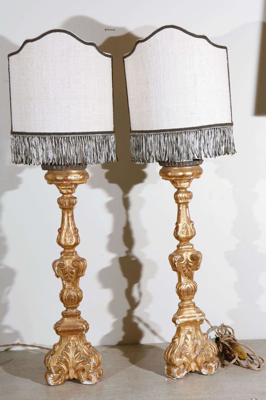 A pair of small carved and gold gilded French candlesticks that have been turned into lamps. The lamps include custom Dagmar shield shades that have silver fringe. They are also fitted with custom wax dripped candles. Newly wired and in working
