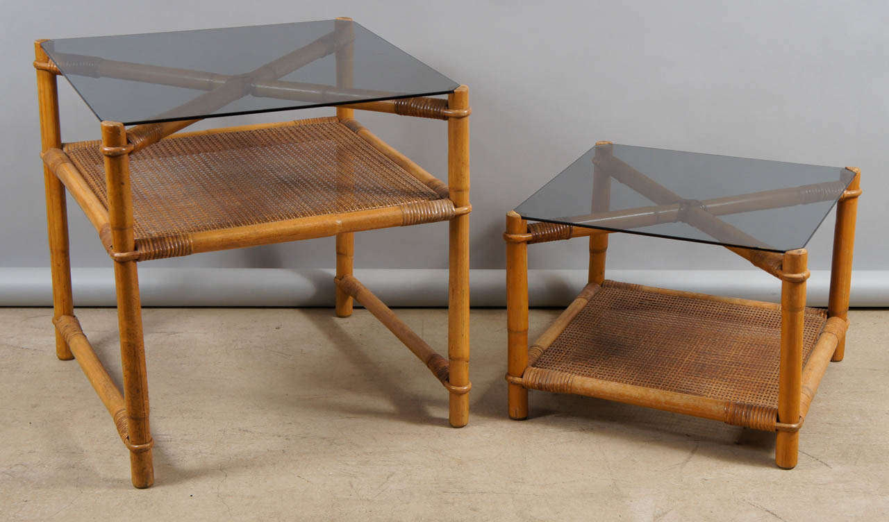 Two end tables made of faux bamboo with rattan shelving and smoked glass tops.