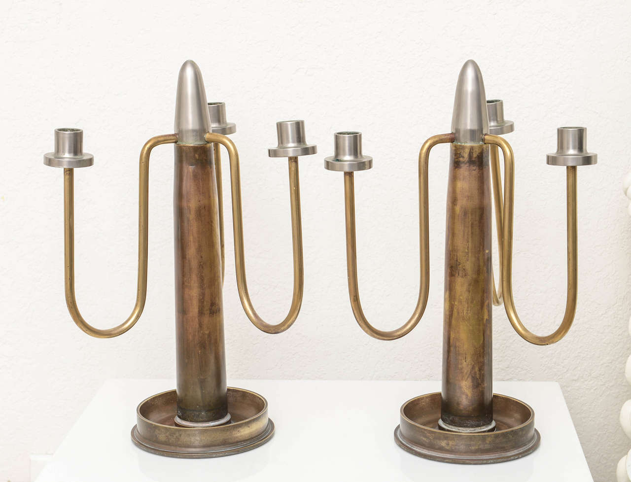 This unusual set of candelabra were created of spent-shell-casing used during WWII. They are constructed of a single shell casing for the central section and the base is the end of an larger shell casing, while the arms are of brass tubing.

 