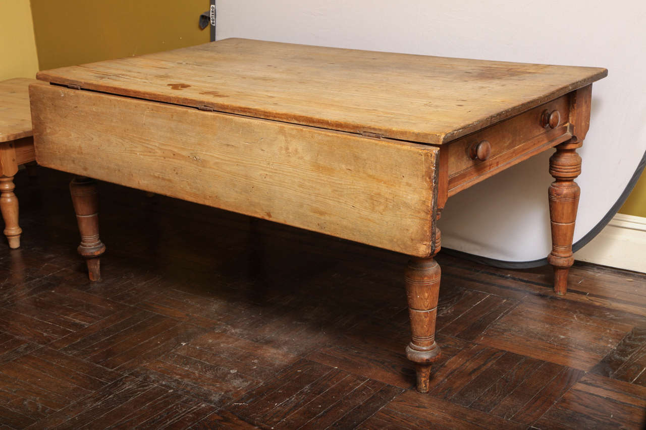 A late Victorian stripped pine kitchen table with one fitted frieze drawer and one extending drop leaf with turned legs.