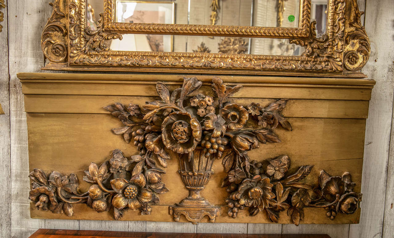 This overdoor panel  of carved wood is  gilded with traces of paint. There is a  central  vase holding a  bouquet of flowers, from which comes  left and right  vines and more flowers.