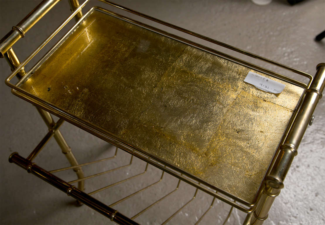 A glamorous Hollywood Regency style gilt brass magazine rack by Jansen, circa 1970s, the top with gilt-glass tier over a compartment to store magazines or books. 