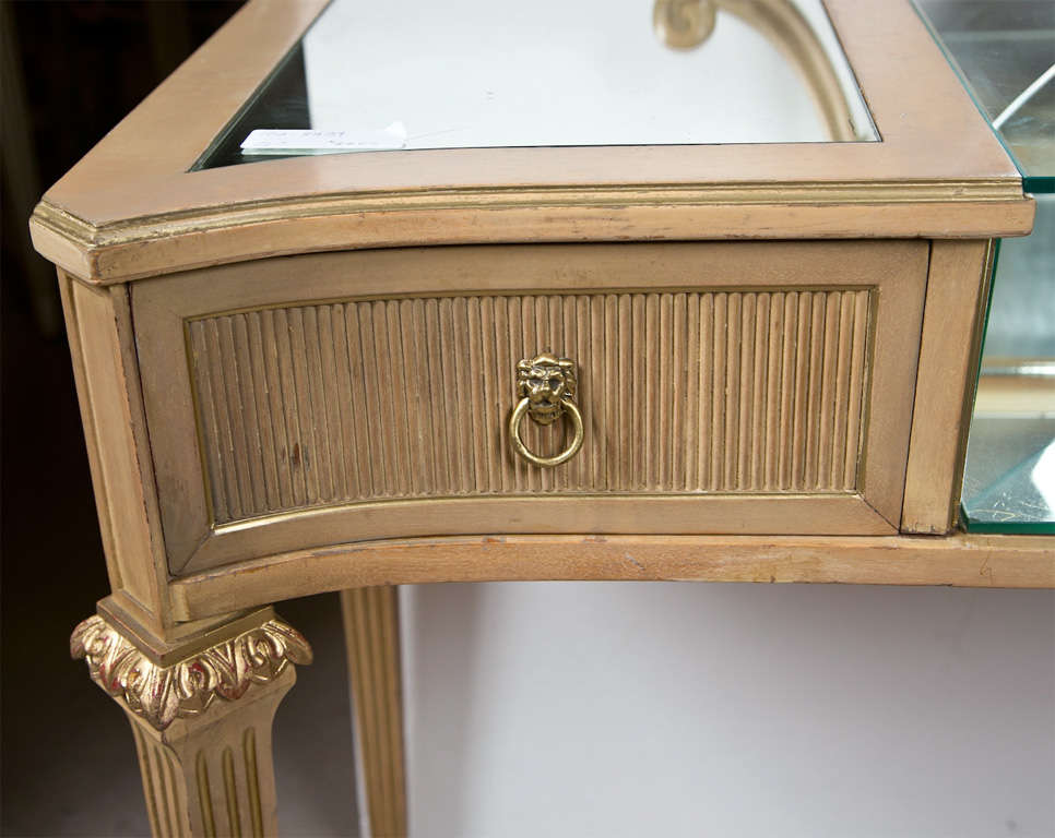 A French painted and slightly distressed vanity by Jansen, circa 1960s, a looking glass raised on a mirrored top with a vitrine in the middle, flanked by two drawers, raised on four tapering fluted legs, ending in toupie feet. 