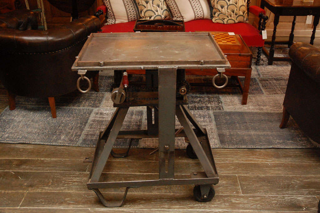 An iron industrial lifting table on wheels with crank mechanism and transport handle. Serves as a side table, stand, occasional table or serving table.
