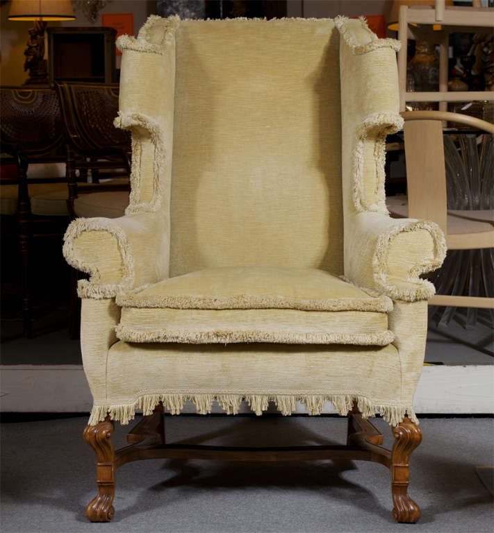 This dramatic wing chair features light walnut carved scrolled knee and foot with finely detailed strecher. The upholstery is a honey colored antiqued cotton velvet with a down cushion and custom brushed fringe detailing. 
This chair was used in