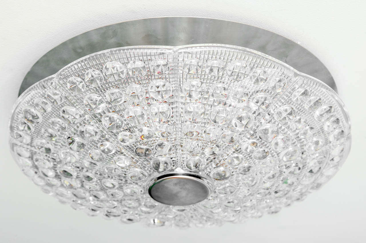 A Swedish Orrefors flush mounted ceiling light. The round molded glass dish with bulls-eyes and texture designed to minimize glare. The lightly scalloped edges upswept and secured with 2 and 3/4 inch flat rosette. The nickel ceiling plate above 6
