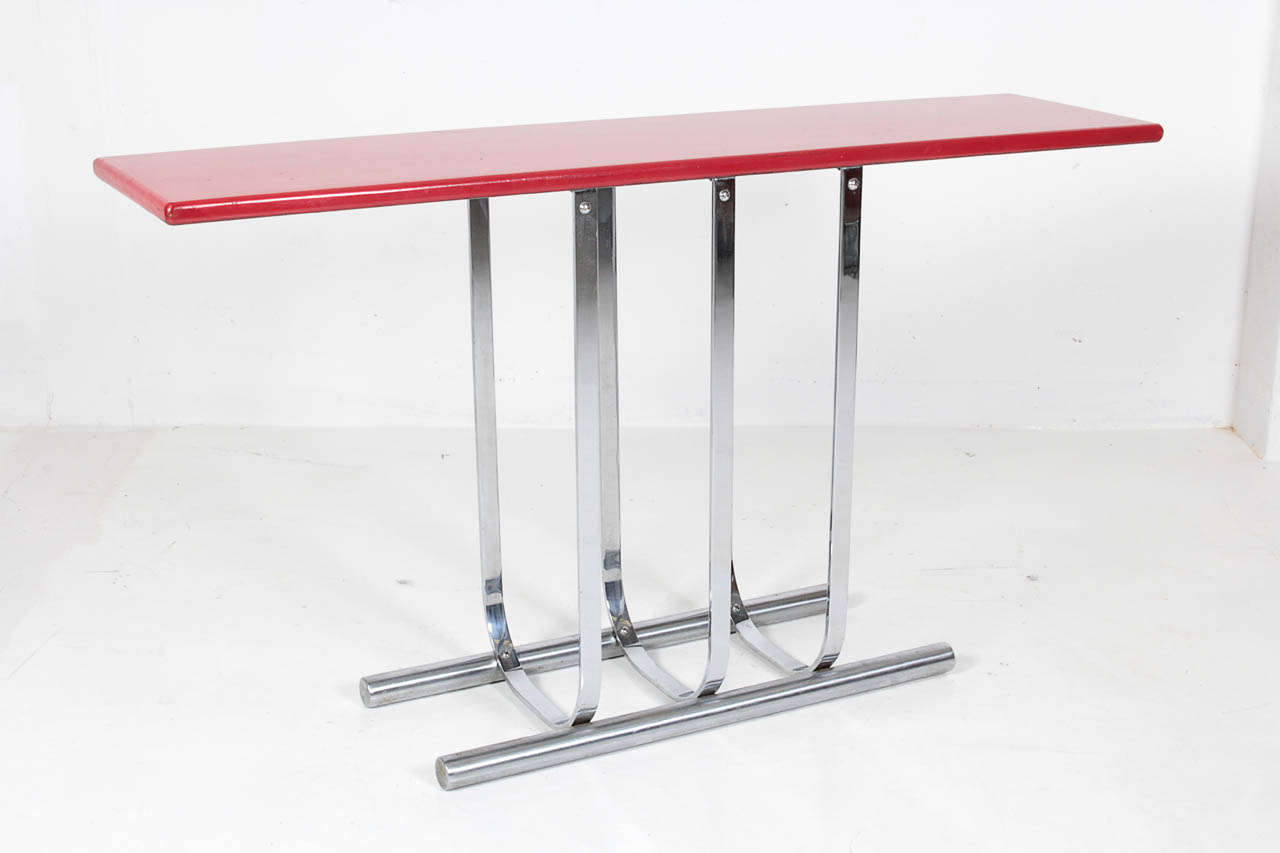 GILBERT ROHDE   (1894-1944)  USA		 	
TROY SUNSHADE COMPANY  Troy, OH

Console Table   c. 1934

Flat band chrome construction mounted to tubular chrome floor supports, red lacquered wood console top in fine original condition 

Marks: Troy