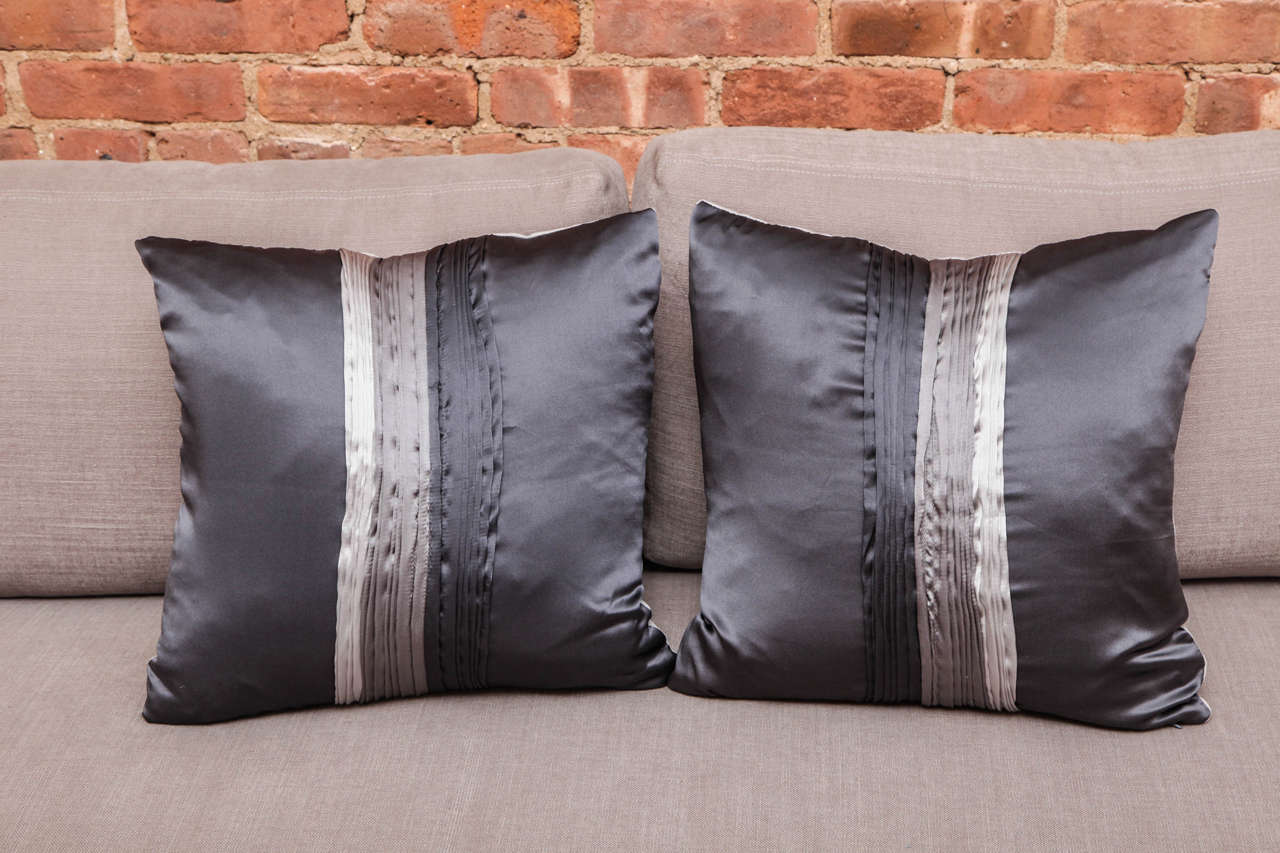 These silky pillows feature quaint detailing, such as the multiple folds in the front of the pillow with gray tonal values, from silver to charcoal colors.
With a mixture of pale silk textile in the back and dark silk textile in the front. It makes