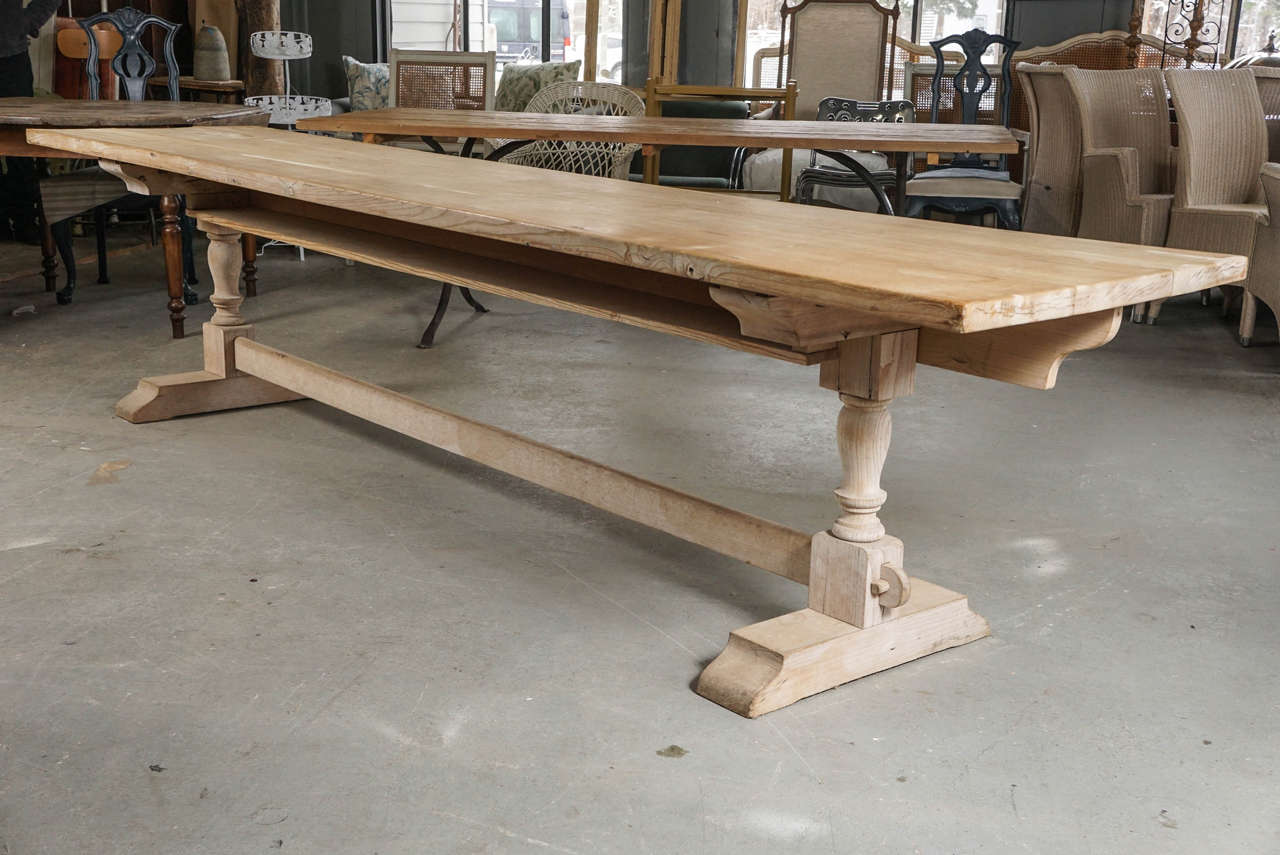 Elegantly rustic plank top, trestle dining table has turned legs sandwiched between a slotted trestle base and T-shaped cross beams of wood and iron at the top. An inset long shelf underneath is fitted between the legs.