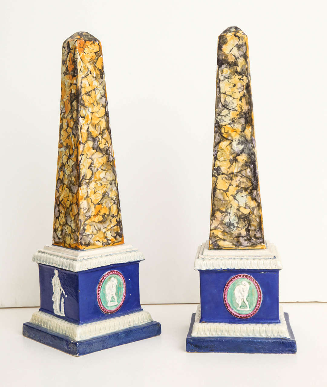 A pair of 19th century English pearlware obelisks with polychrome faux marbleized decoration, the bases decorated with neoclassical figures in relief.