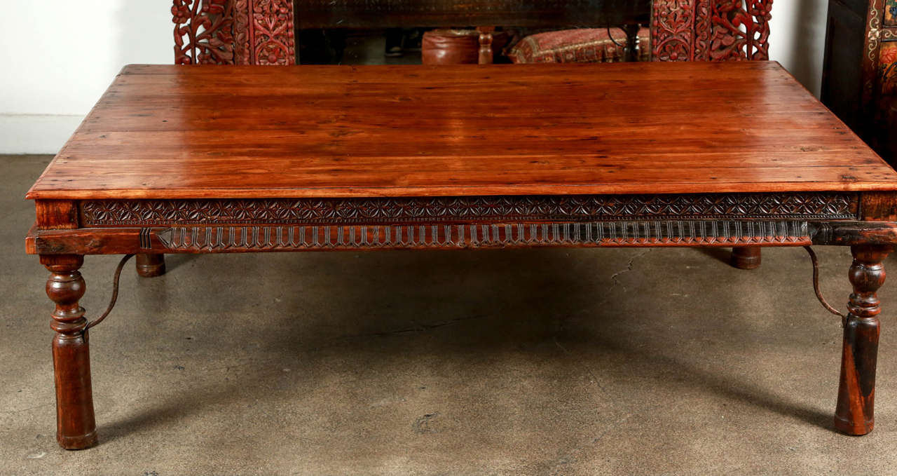 Anglo-Indian coffee table solid teakwood. Four planks with large rounded nailheads and metal accents support, very nicely carved legs and sides and the corners are reinforced with metal iron pieces.