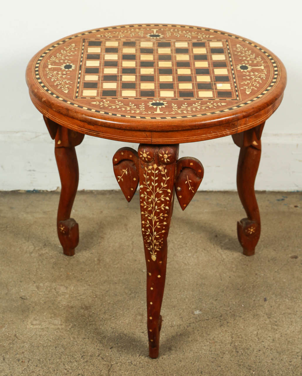 Elegant Anglo Indian round side table delicately handcrafted and inlaid with mother-of-pearl and ebony. 
Floral Moorish inlay designs and elephant head on the three legs.
With chest board design on top.
Vintage wooden game chest table.