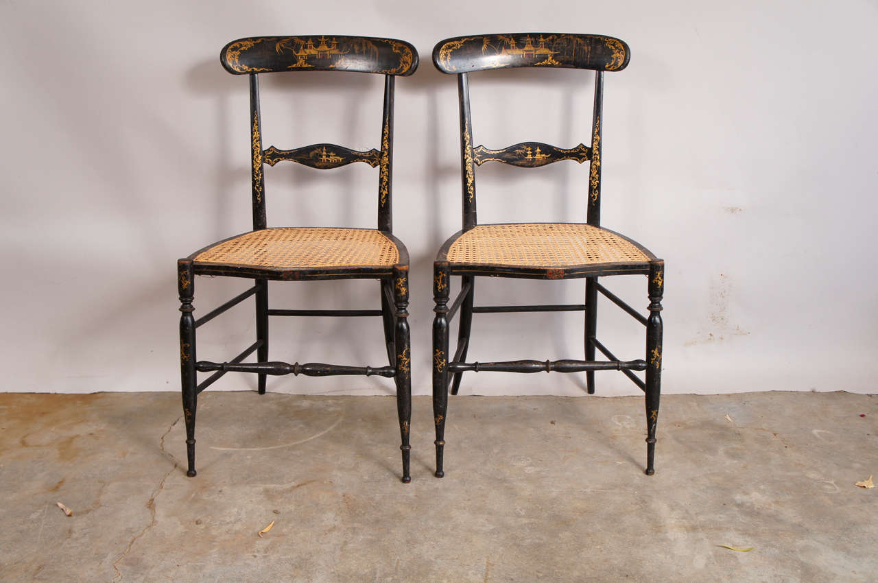 Fantastic pair of Chinoise side chairs. Black lacquer over wood with lovely gold painted detail. Delicate refined form with hand caning give these chairs a stunning decorative appeal.