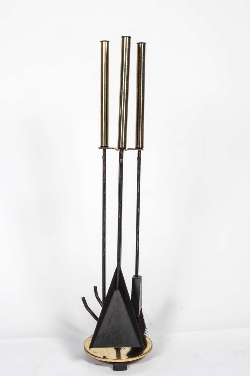Set of black metal fireplace tools accented in polished brass.  USA, circa 1960. Includes stand with round base and poker, shovel and brush.  Base and tool handles have brass finish.