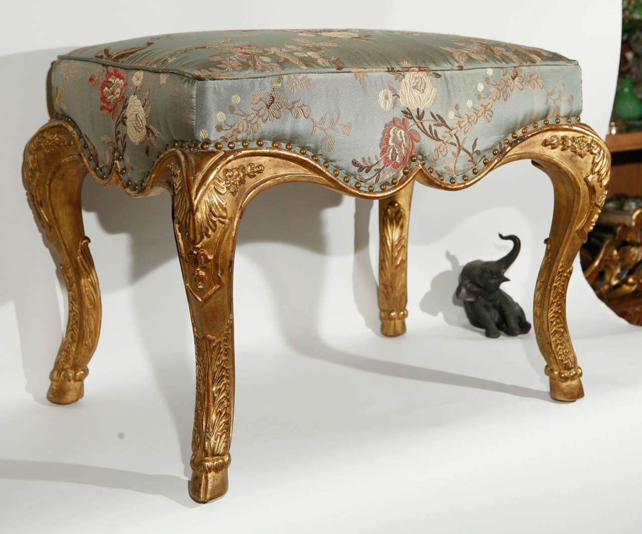 Italian style 22-karat giltwood stool with hoof feet upholstered in silk fabric. This is stool is not antique.
