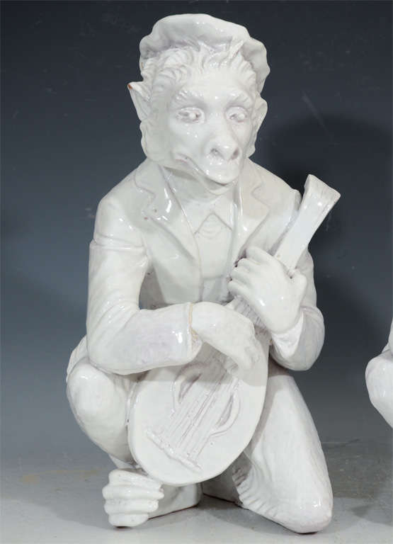 A pair of Chine de Blanc glazed terracotta monkey sculptures; each depicted with an instrument.