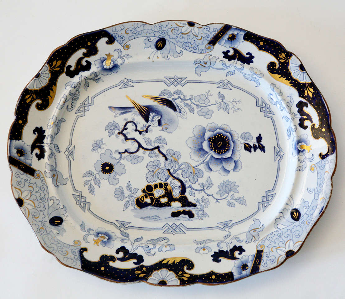 Soft blue, cobalt blue and gilt platter on white background depicting a bird resting on a branch.