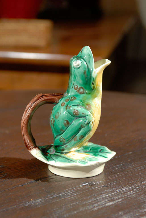 This is a whimsical frog pitcher.  The open mouth spout and twig handle lend to the creative pitcher or jug.  The frog sits upon a lily leaf.  The colors are vibrant and charming.  This jug is by the English majolica producers, Edward Steele. 