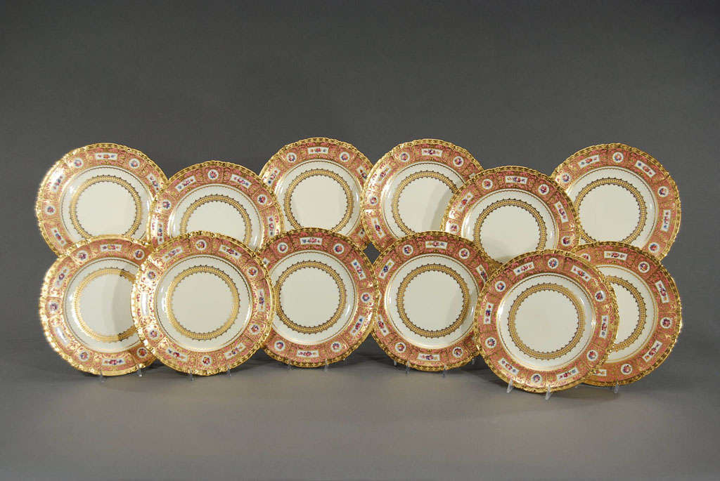 This rare set of 12 dinner plates made by Royal Crown Derby for Tiffany, exemplifies their fabulous workmanship and attention to detail. The shaped edge is embellished with raised paste gold, framing the border in a soft rose and alternating