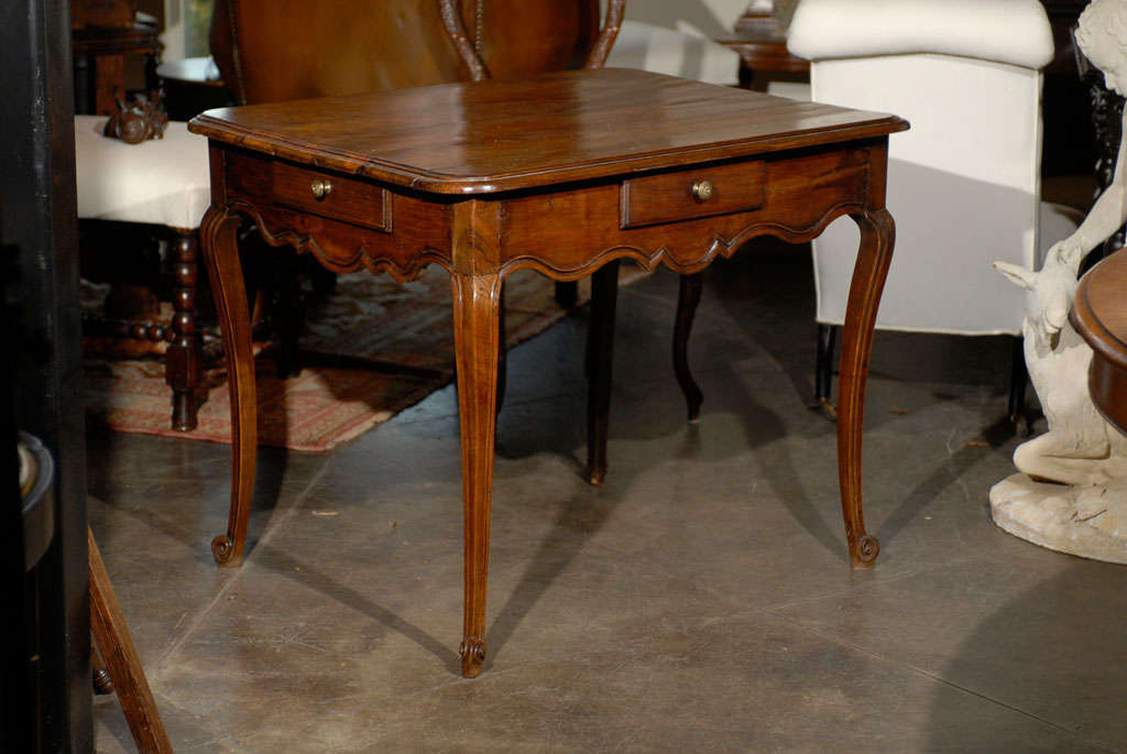 A French Louis XV style walnut side table from the mid-19th century. This French side table features a rectangular top with beveled edges and rounded corners over four small drawers placed on each side of the apron. This apron attracts all the