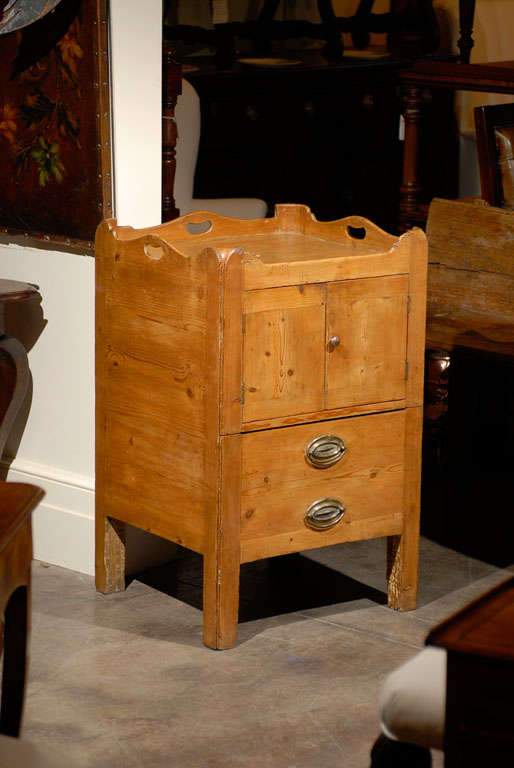 This lovely English pine commode from the early 19th century features a pierced tray top over a double door and a single drawer. The doors open up to reveal a red painted storage. The maker used an ingenious trick in the lower section, placing two