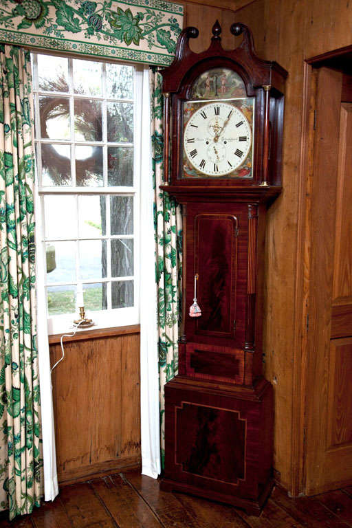 This tall case clock is beautifully crafted in mahogany and features numerous details that make it a desirable timepiece. From the swan neck pediment with full column supports to the satinwood inlaid quarter columns on the waist, the workmanship is
