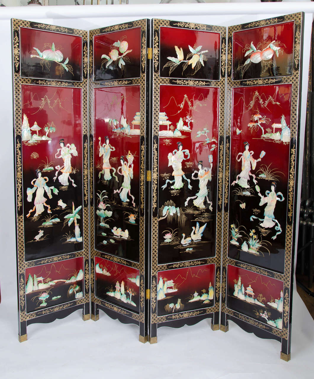 A striking vintage coromandel screen. This room divider has a rich, red and black background with mother of pearl decoration. One side of the screen features floral, garden and landscape scenes separated by strips of geometric patterns. The other
