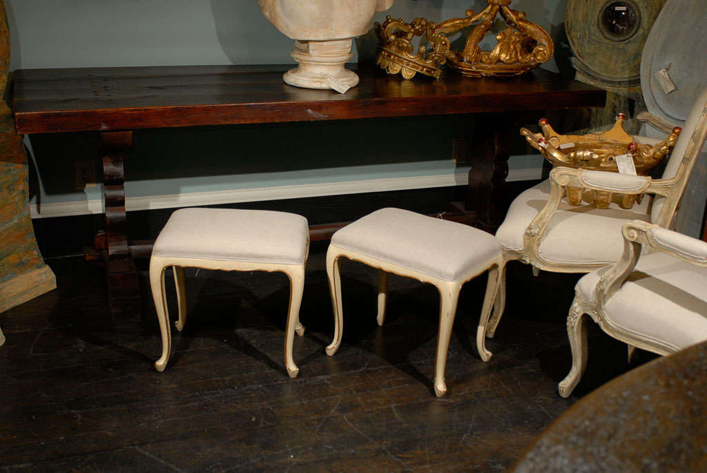 A pair of French Louis XV style stools. This pair of soft white and cream painted stools with original finish is raised on nice cabriole legs. The gilded outline of these French stools as well as the slight scalloping on the skirt provides a