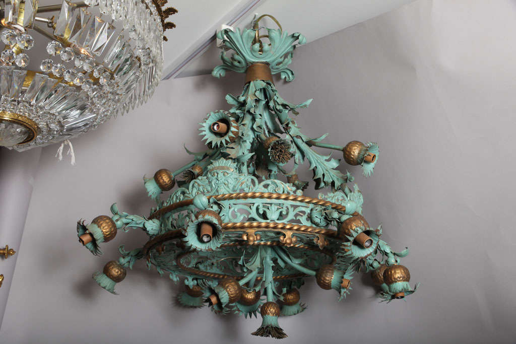 An English Arts & Crafts style chandelier with verdigris painted metal frame the open fret center ring with metal braid edge, the upper and center sections with upswept bouquets of thistle branches and leaves alternating flower heads with concealed
