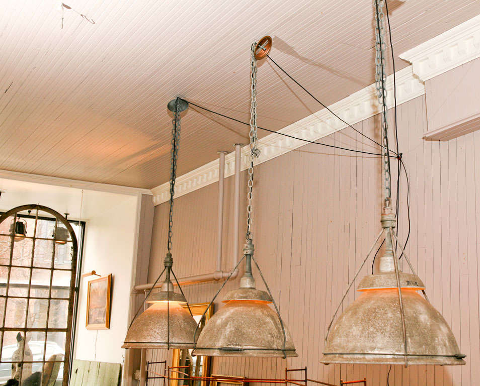 three holophane pendant lamps <br />
glass reflector interior<br />
pitted exterior surface <br />
adjustable top tier to release heat and light<br />
shade hangs from three supporting rods<br />
metal clamp rings the rods together at rim<br