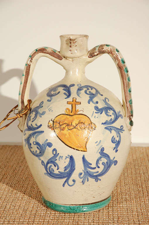 Multi-colored glazed pottery. Double arm vessel with sacred heart design.