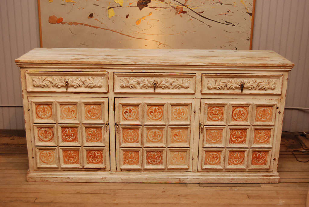 shabby chic off white sideboard with sepia colored tile doors<br />
three drawers with foliate carving<br />
over three nine panel doors<br />
cotter pin hinges<br />
drop pull hardware<br />
interior shelf