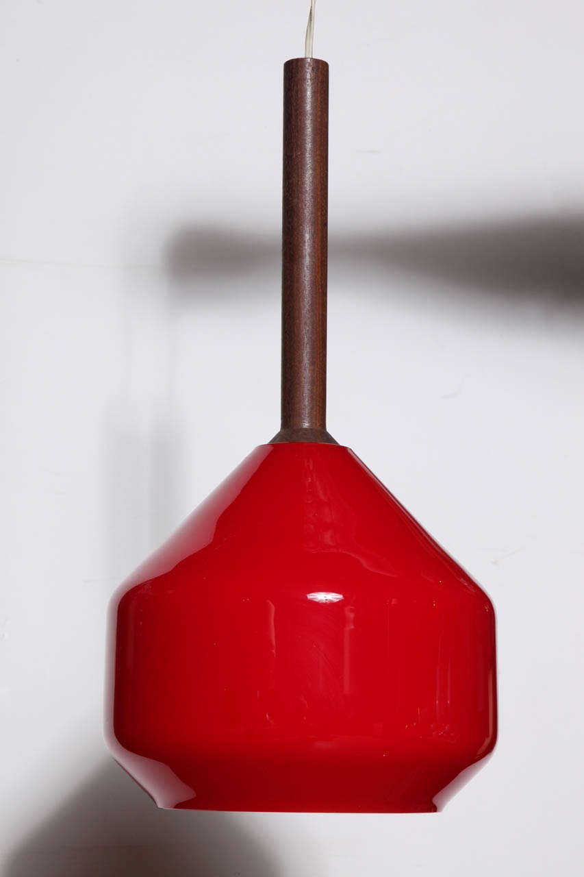 Scandinavian Modern Tapio Wirkkala Teak hanging pendant with red glass Vistosi shade. Featuring a suspended turned teak rod supporting a rounded, angular Tomato Red glass Vistosi shade with White interior. Warm. Complimentary light. With 6.5