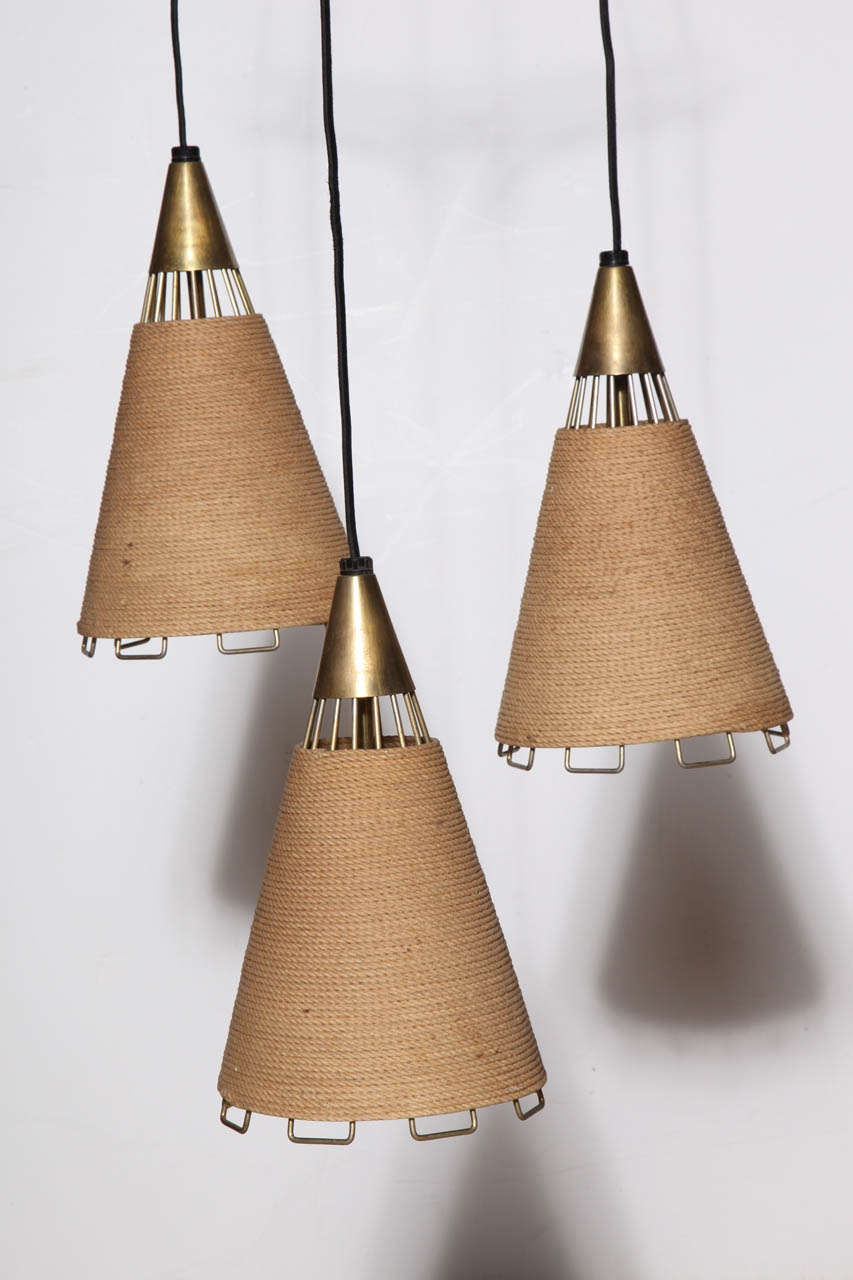 Thomas Industries Moe Light, Cordette Series Whirl Cord and Brass Hanging Lamps. Featuring three varied height, horizontally wrapped laminated Tan Cotton Cord cone pendants with Brass wire and cap details. Complimentary light. Warm. Mobile. Breezy.
