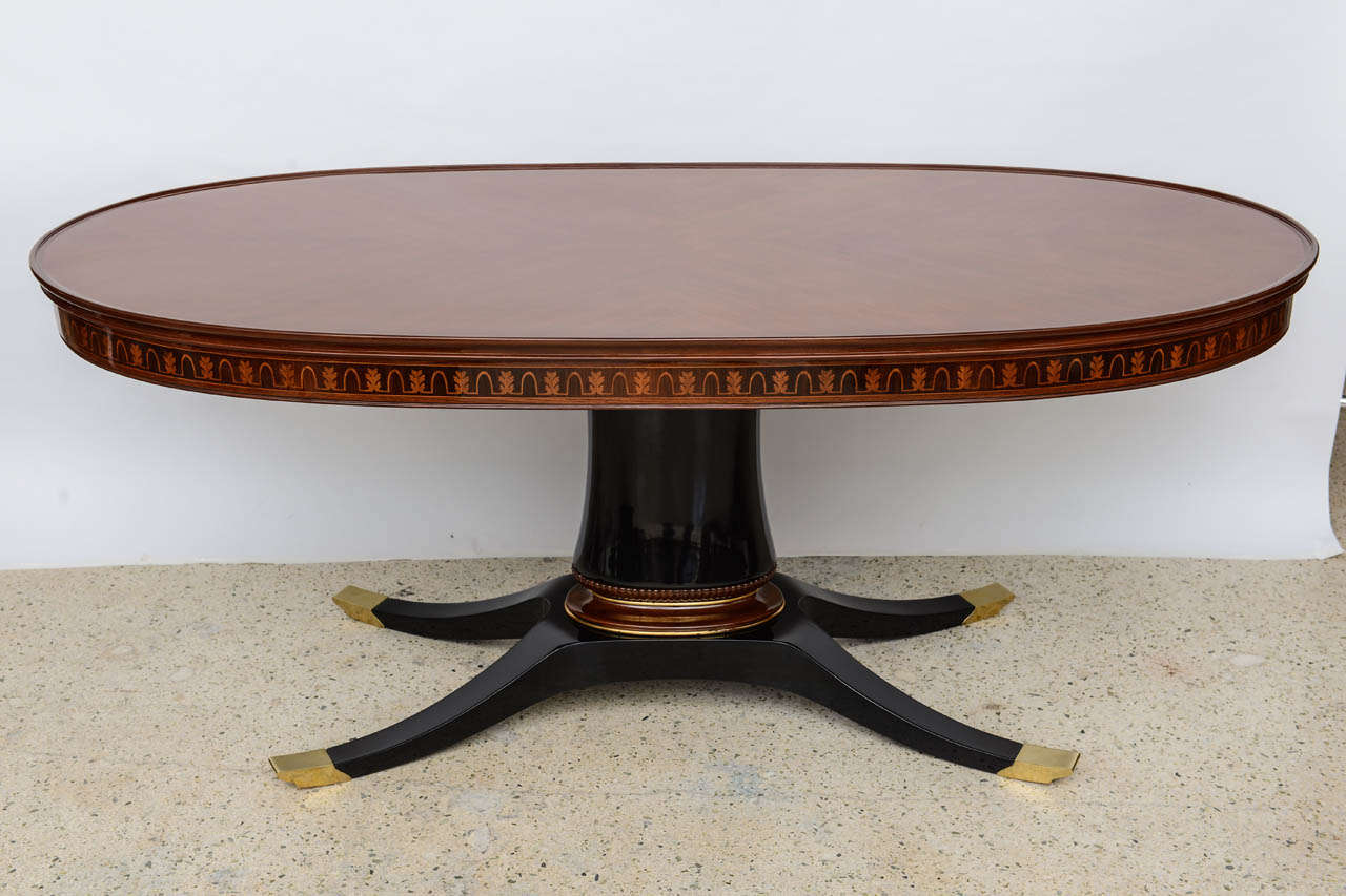 The oval top veneered au quatre faces, with an elaborately inlaid frieze on an ebonised and parcel gilt, brass mounted columnar base and quadripartite feet ending in brass caps.