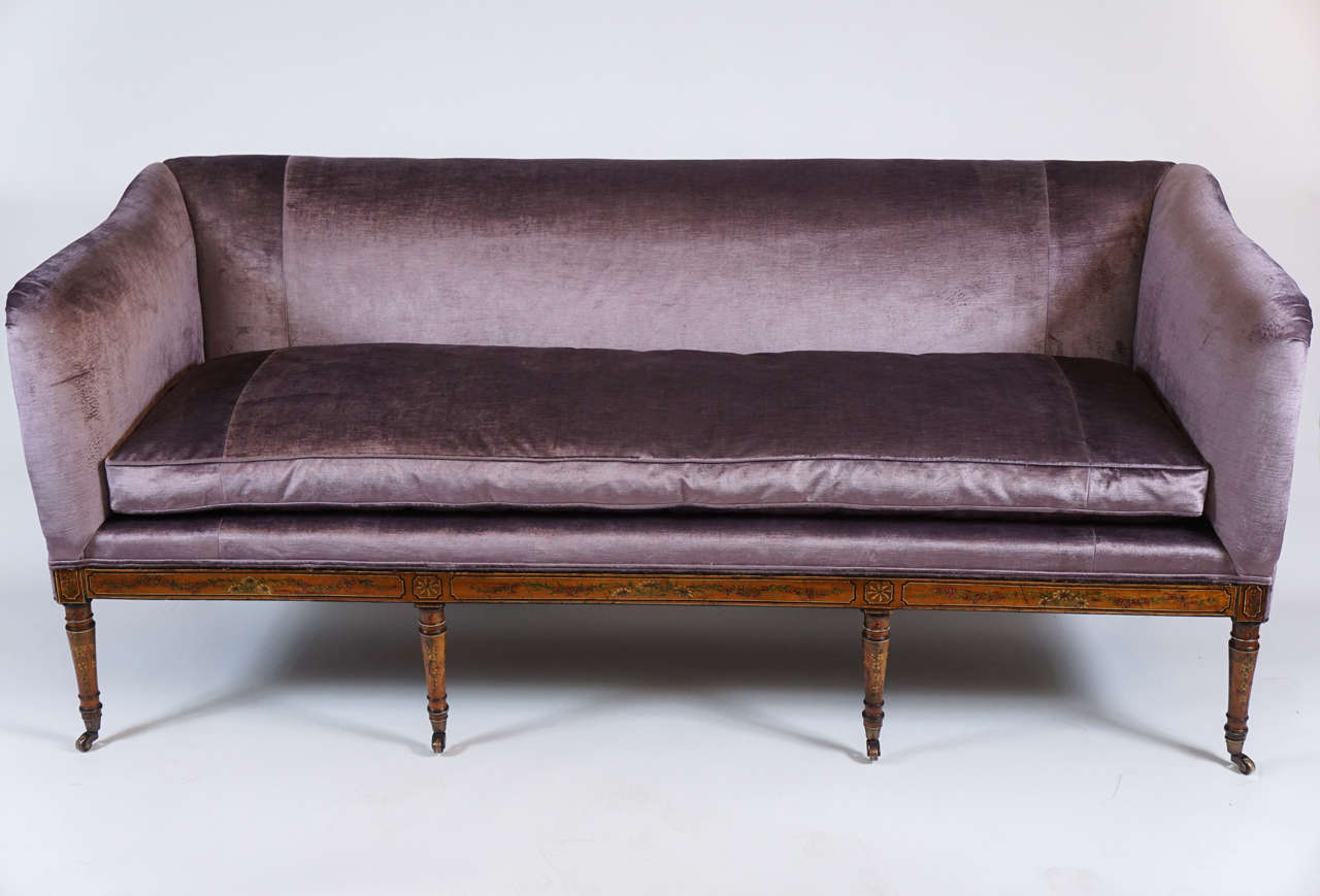 Rare English George III period sofa having floral and geometric painted motifs in the style of Angelica Kauffman on satinwood frame with turned tapering front legs and splayed rear legs all on casters, circa 1795. Recently upholstered in lilac