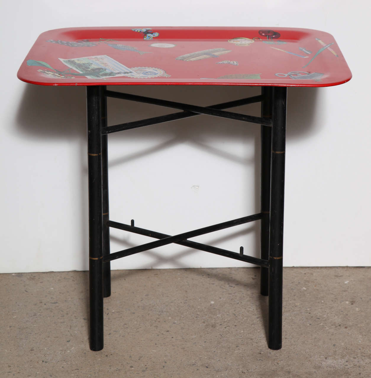 Piero Fornasetti Trompe L'Oeil Occasional Table, Butlers Tray Table. Featuring a Red enameled lipped rectangular Aluminum tray with colorful lithographic transfer prints and folding Black lacquered wood stand with gold details. Red background
