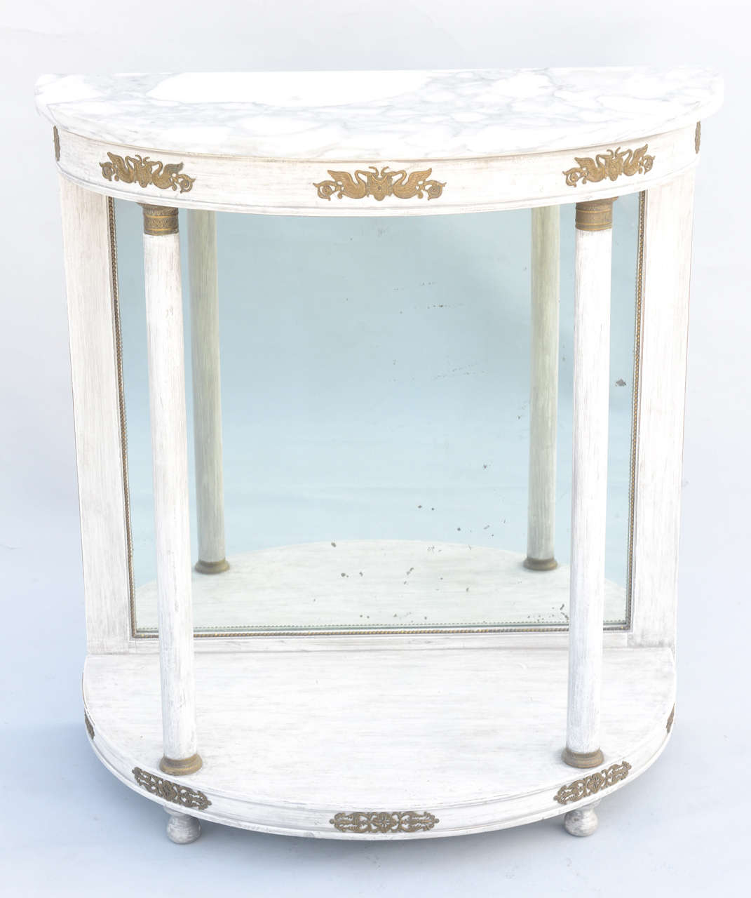 Demilune console, with top of Carrara marble, on painted base, having two round columns supporting its ormolu embellished apron and conforming platform, with a back of distressed mirrorplate framed with cockbeading, raised on bun feet.

Stock ID:
