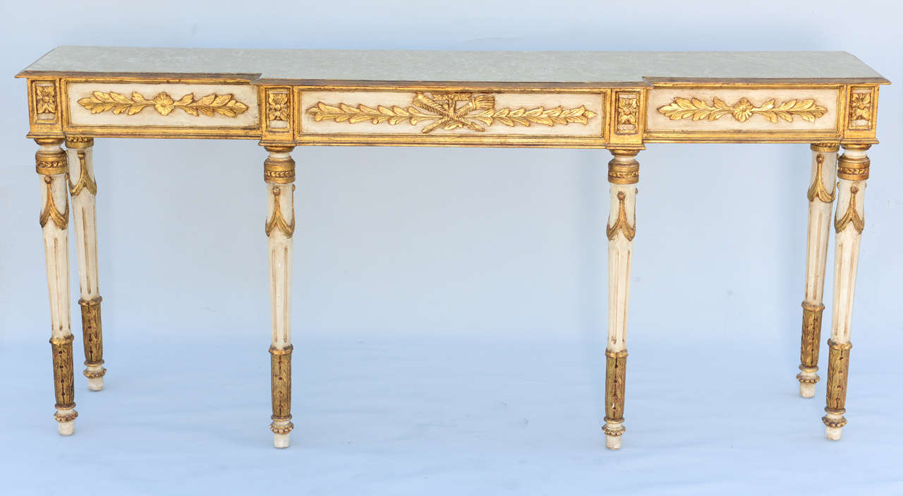 Console table, long and narrow proportions, having a faux painted breakfront top, in Louis XVI taste, on table with distressed painted and parcel gilt finish, its fielded apron out carved with foliate carving, raised on round stop-fluted legs.