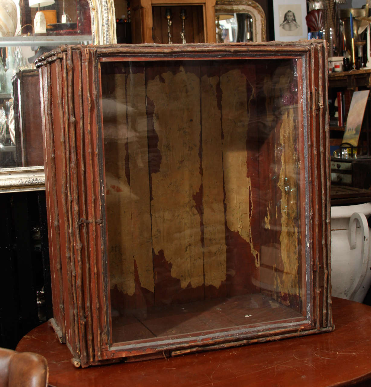 Large wood and branch trimmed display case with old glass hinged door. Remnants of old wallpaper on back inside of case. This case is impressive on a table and looks equally good on the floor used like a chest or tall side table. Great color and