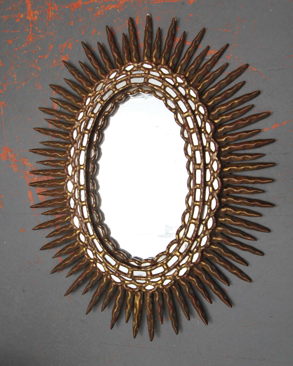 Oval sunburst mirror of gilded wood frame with rich brick red undertones.