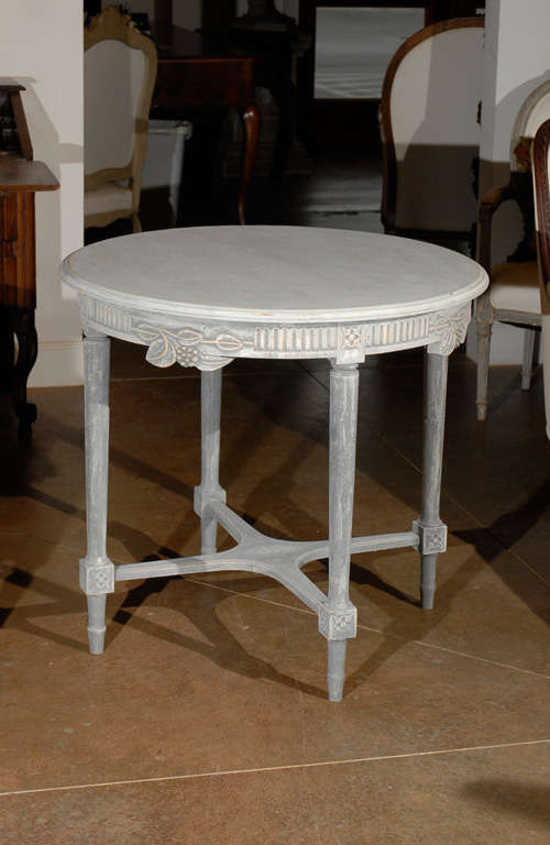 A Swedish painted round centre table with foliage and berries carved motifs, scoop patterns and Saint-Andrew cross stretcher from the, 19th century. This Swedish painted table features a simple circular top sitting above a round apron, adorned with