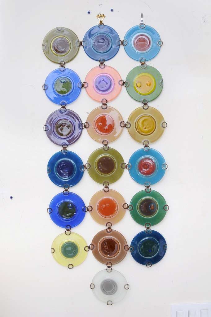 This is a great array of luscious different colored round glass disks done by the famous glass house of Michael and Frances Higgins. This can either be a wall screen or hanging screen all reflecting beautiful play of color and light. These rondeles