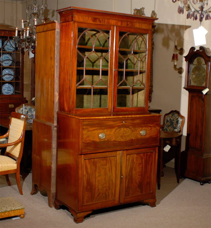An English figured mahogany secretary bookcase with moulded cornice, glazed doors with arched sash work, pullout drawer enclosing writing surface, small drawers and pigeonholes. Below are cabinet doors with interior shelf. All resting on ogee feet.