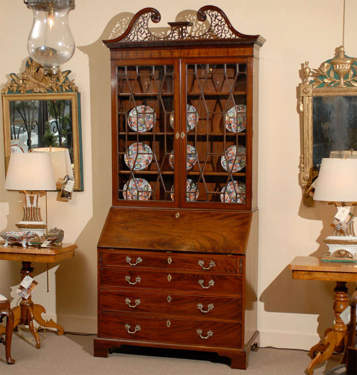A mahogany bureau bookcase with swan neck pediment, cabinet with geometric sash work, slant front enclosed desk with pigeon holes and fitted interior drawers. Below are 4 drawers with brass pulls resting on bracket feet.  The pediment is new.