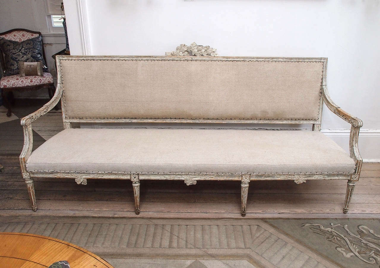 Louis XVI style settee with painted wooden frame. Fluted legs and Louis XVI style carvings accented with appliques with acanthus leaves and berries. Upholstered in muslin.