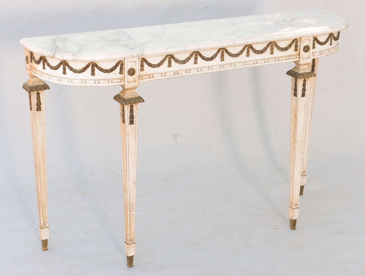 Directoire style D-shaped console table, having distressed painted finish, white marble top, its apron decorated with bronze swags, raised on four tapering square legs.