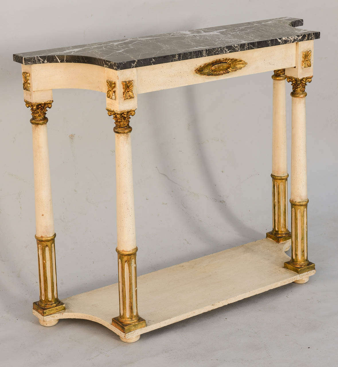 Console table, painted white with parcel gilt, having a  black veined marble top with concave sides, raised on four round fluted legs, headed with Corinthian capitals, joined by a shelf stretcher. 

Stock ID: D6988